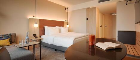 A hotel room with a bed, bedside table, and a round table with a book.
