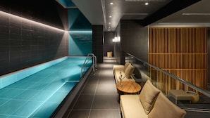 A modern indoor pool area with a seating area and a wooden panel wall. - Adina Apartment Hotel Stuttgart (Stuttgart)