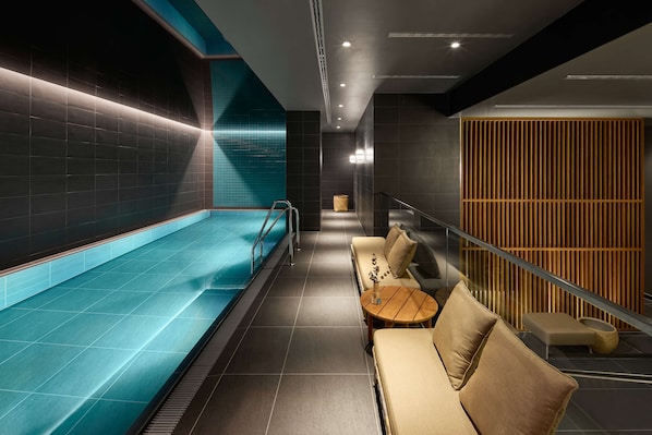 Un área de piscina interior moderna con zona de estar y pared de paneles de madera.