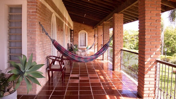 A covered outdoor area with a brick wall, a hammock, and a tiled floor. - Chacara Giovaninha, located in Serra dos Cocais.  (Valinhos)