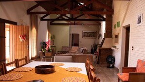 A dining area with a wooden table set for six, surrounded by wooden chairs. A brick fireplace is visible in the background. - Chacara Giovaninha, located in Serra dos Cocais.  (Valinhos)