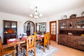 Un coin repas avec une table en bois, des chaises et un lustre. On y trouve également un buffet sur lequel sont disposés de la vaisselle.