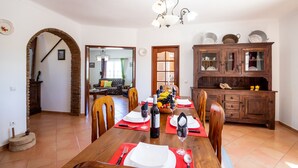 A dining room with a wooden table set for six, a chandelier, and a kitchen area with a wooden cabinet. - Elegant villa with BBQ and heatble pool (Armação de Pêra)