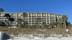 Un hôtel à plusieurs étages, doté de balcons, de palmiers et d’une plage de sable au premier plan.