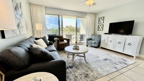 Un salon moderne avec un canapé, des fauteuils, une table basse, un téléviseur et un balcon offrant une vue agréable.