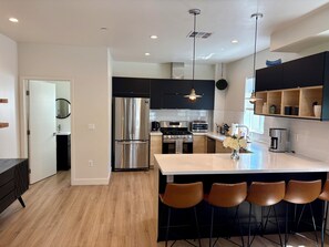 A modern kitchen with a central island, stainless steel appliances, and black bar stools.