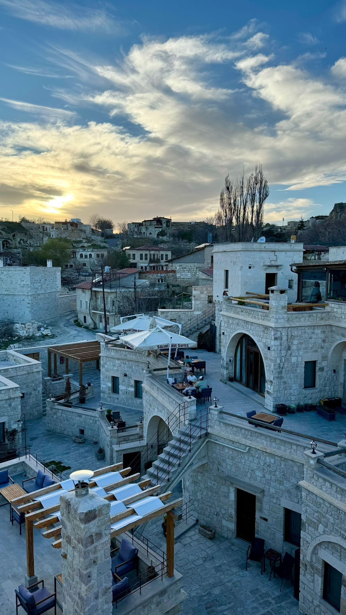 A courtyard with stone buildings, outdoor seating, and a view of the sunset.