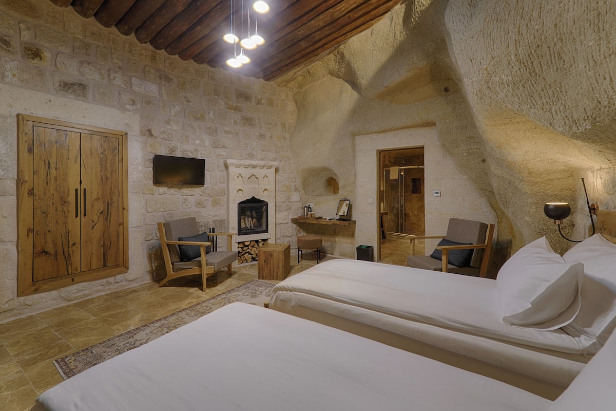 A rustic stone-walled bedroom with two beds, wooden furniture, and a fireplace.