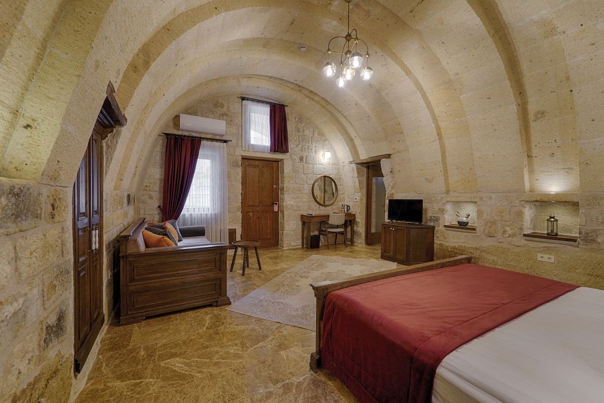 A bedroom with a stone vaulted ceiling, a bed, a desk, and a television.