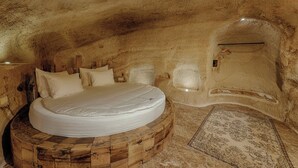 A circular wooden bed in a cave-like room with a rustic, natural stone floor and a patterned rug. - Solem Cave Suites (Ürgüp)