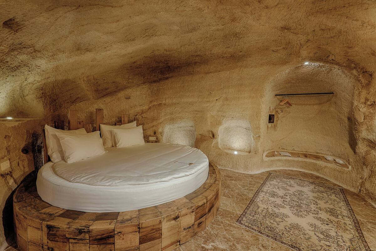 A circular wooden bed in a cave-like room with a rustic, natural stone floor and a patterned rug.