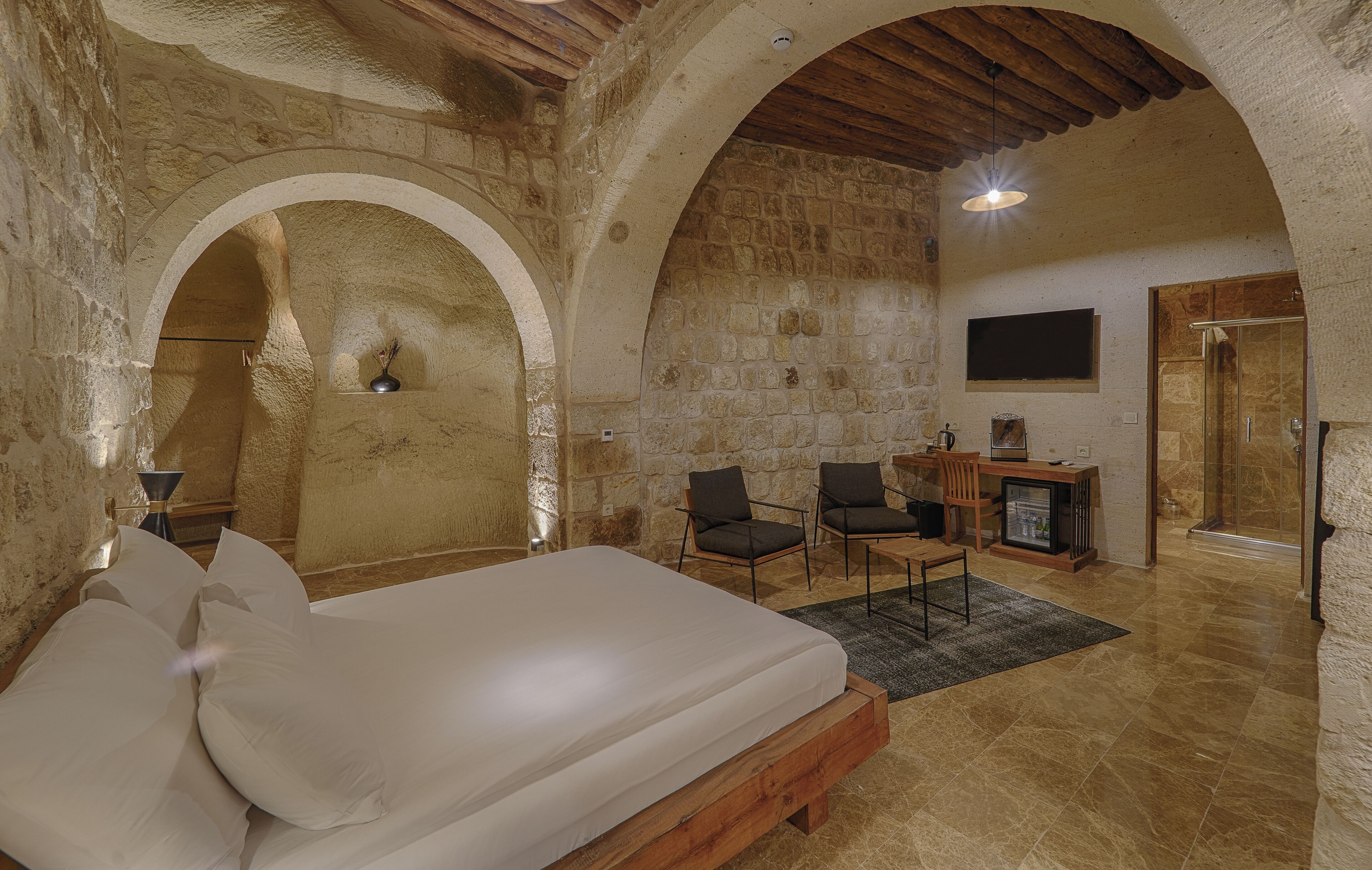 A rustic bedroom with a large bed, stone walls, wooden beams, and a stone fireplace.