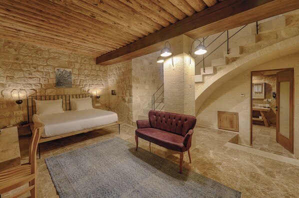 Un dormitorio con una cama, un sofá rojo, una pared de piedra y una escalera.