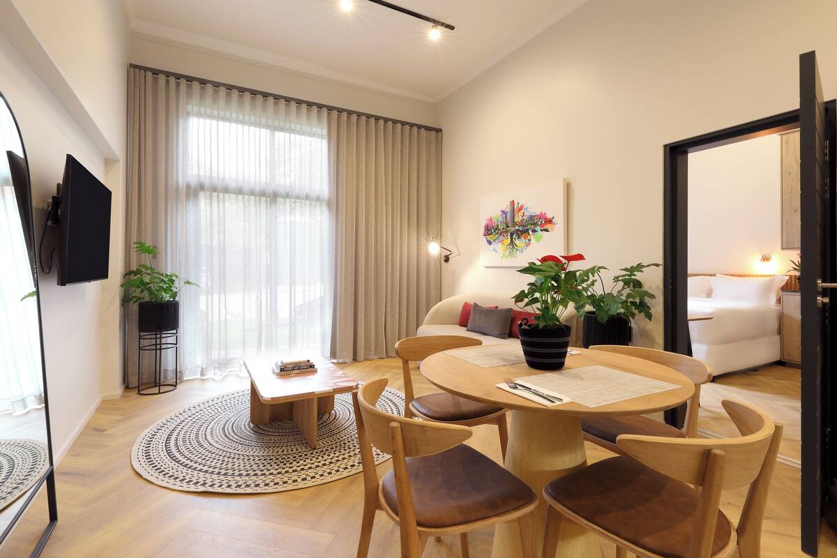 Una sala moderna con comedor, televisor de pantalla plana en la pared, sofá con un cojín rojo y una planta en maceta.