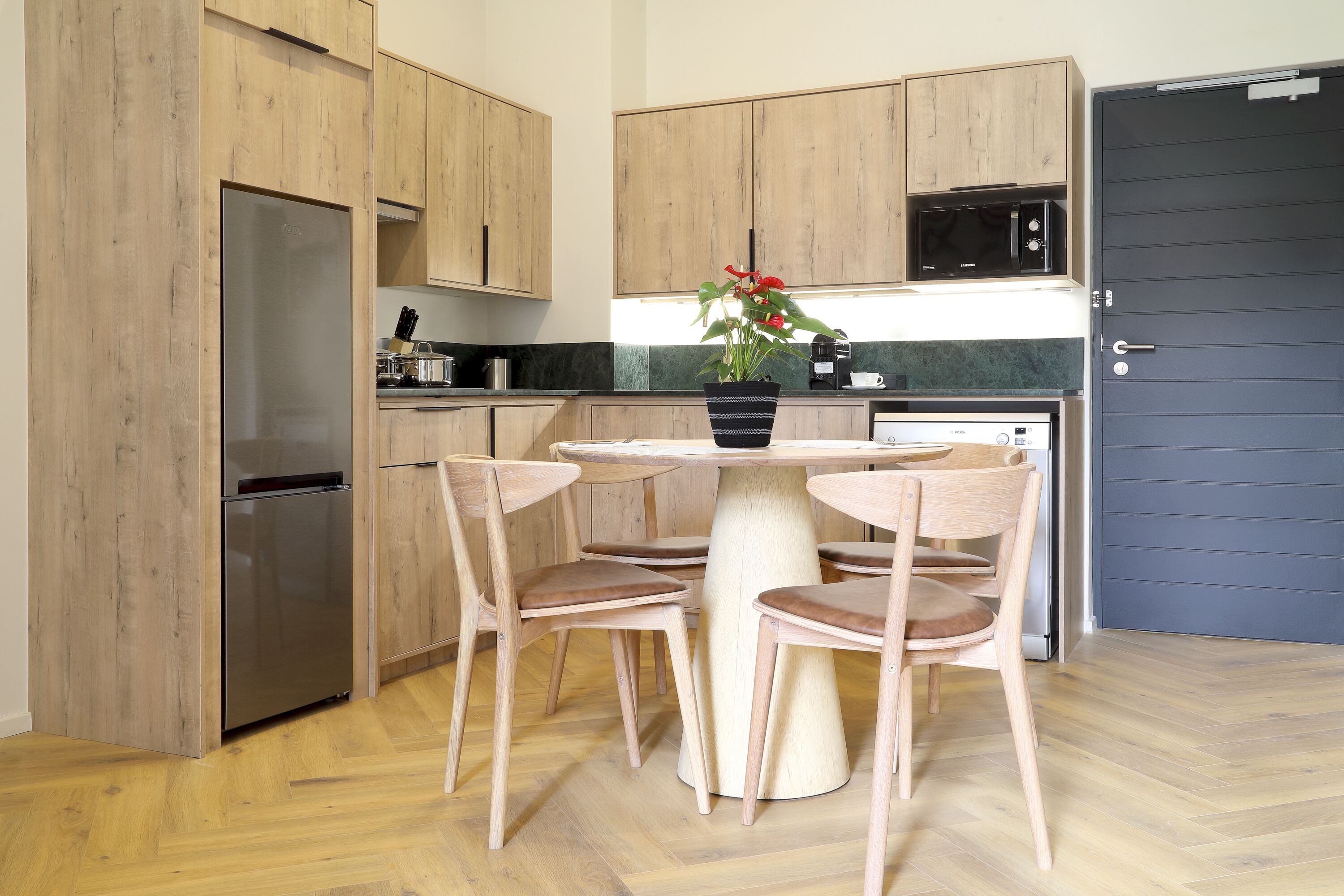 A modern kitchen with wooden cabinets, a stainless steel refrigerator, a microwave, and a dining table with four chairs.