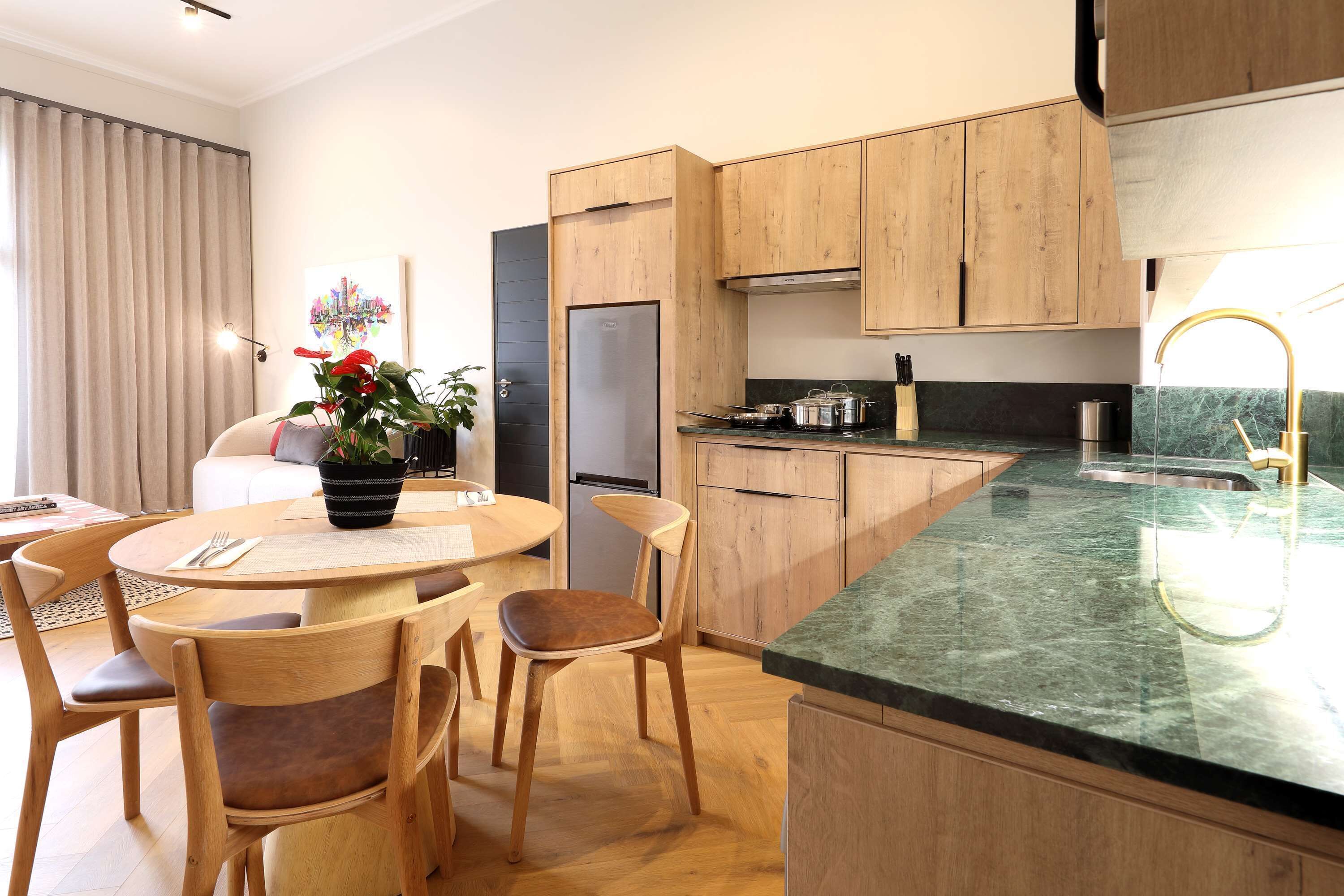 A modern kitchen with wooden cabinets, a marble countertop, and a dining area with wooden chairs and a table.