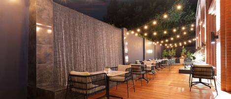 An outdoor patio with wooden flooring, black metal chairs, and tables.
