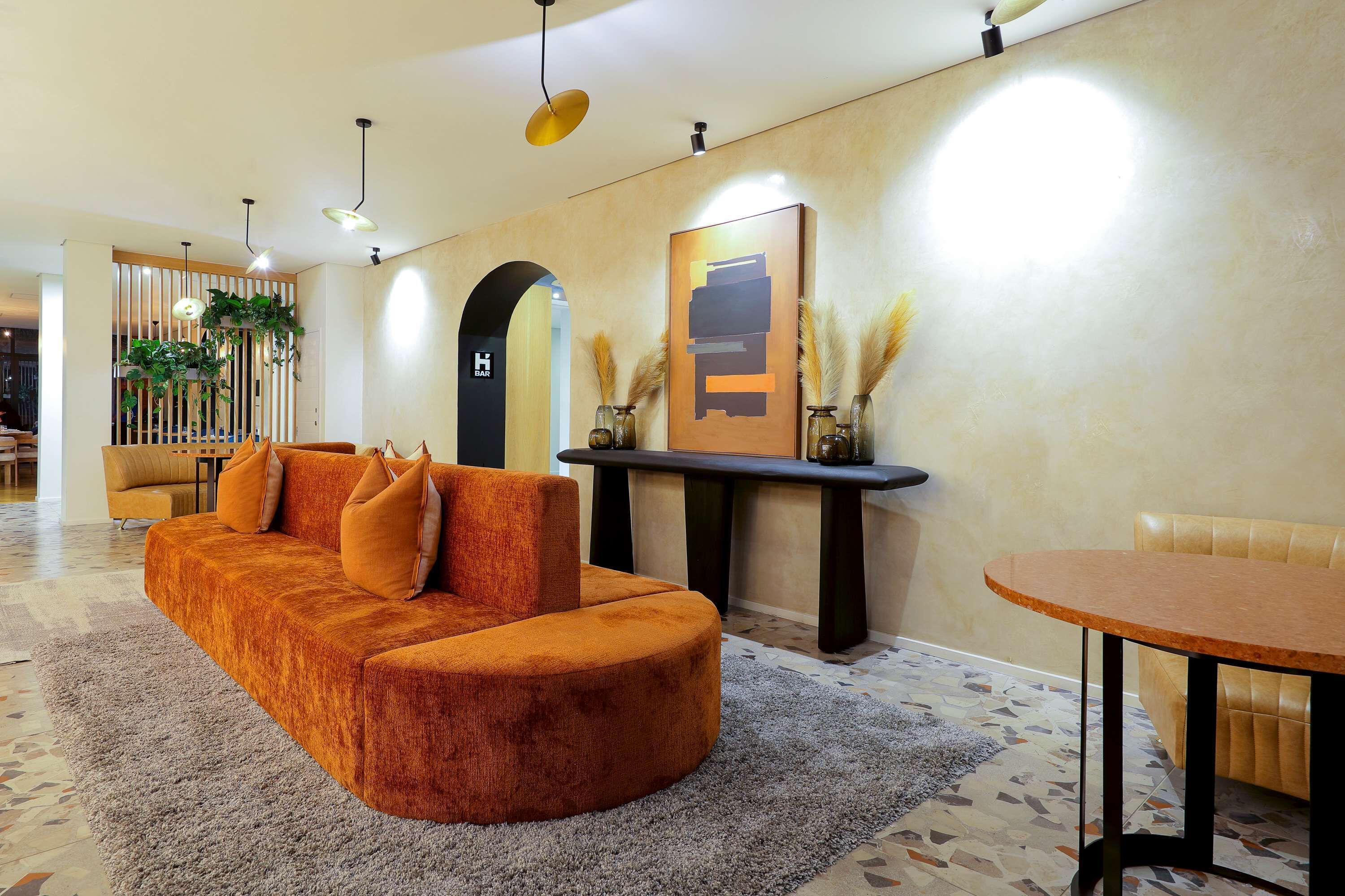 A modern lobby with a curved orange sofa, a round wooden table, and a decorative wall with a framed artwork.