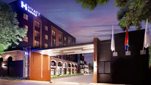 A modern hotel entrance with a prominent sign, a covered walkway, and flags.