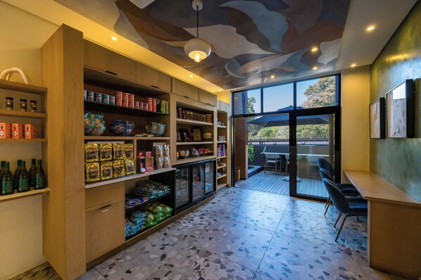 A modern interior with wooden shelving stocked with snacks and beverages, a tiled floor, and a view to an outdoor seating area.