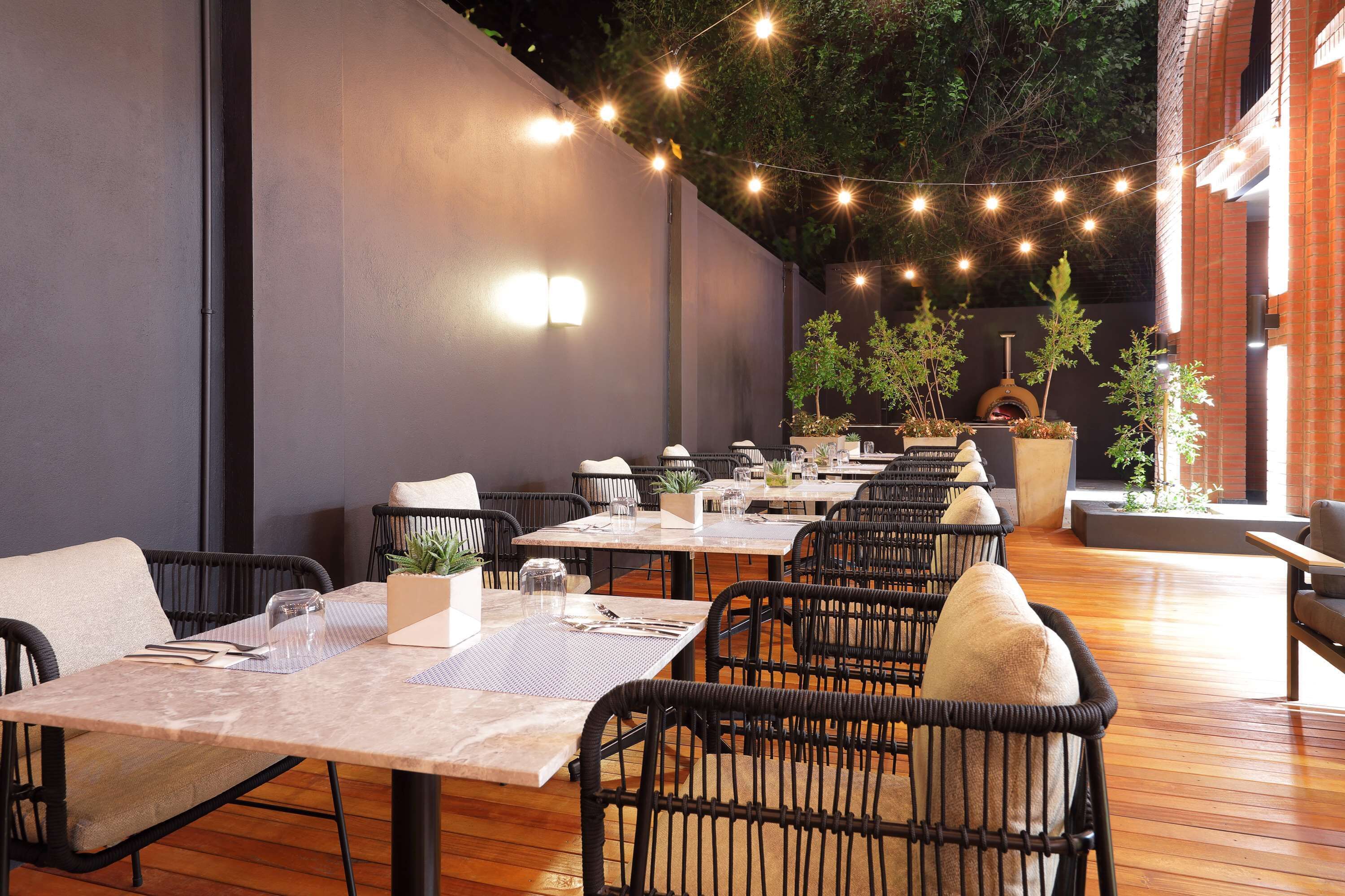 An outdoor dining area with multiple tables and chairs, string lights, and potted plants.