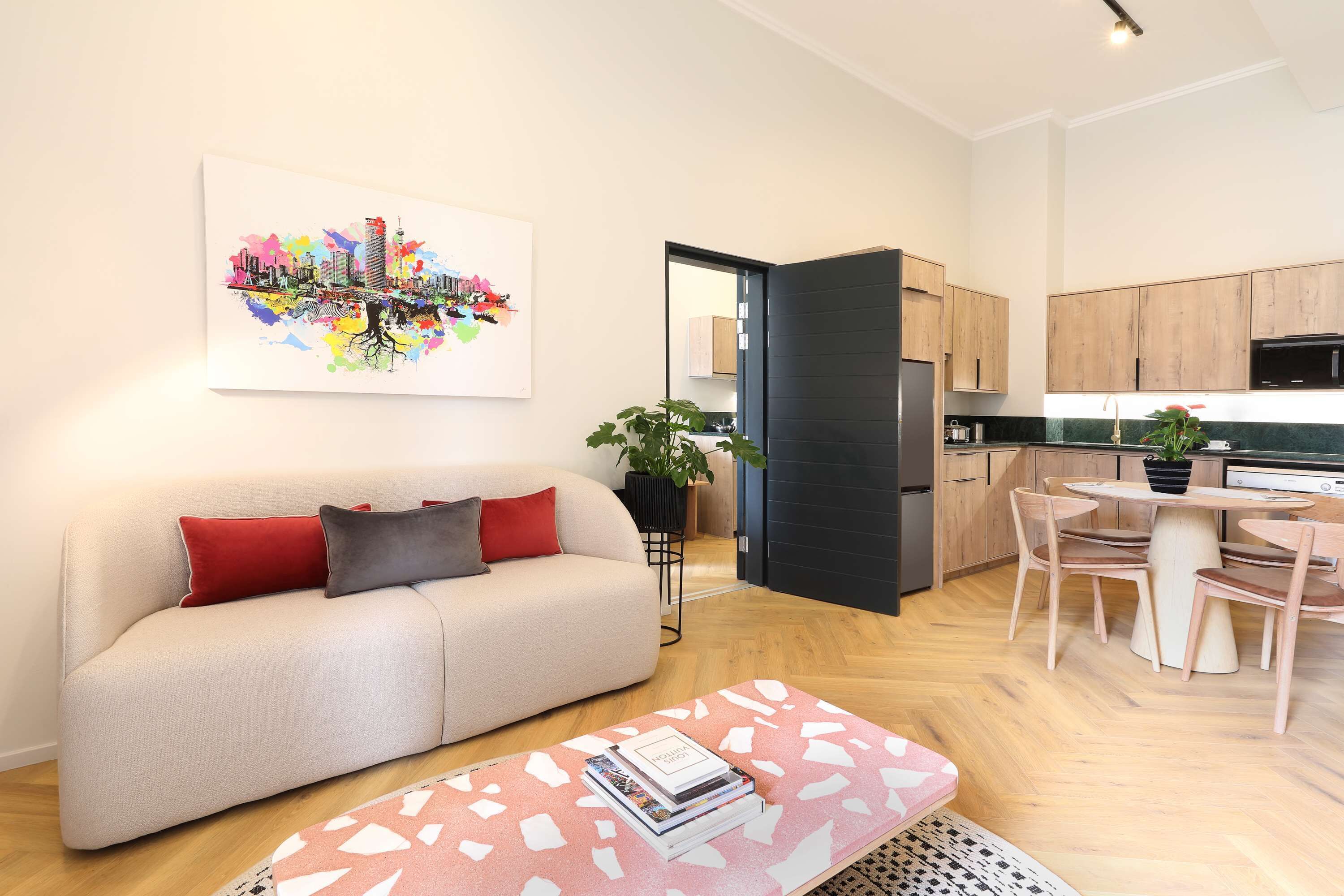 A modern apartment with a living area featuring a sofa, a coffee table with books, and a cityscape artwork.