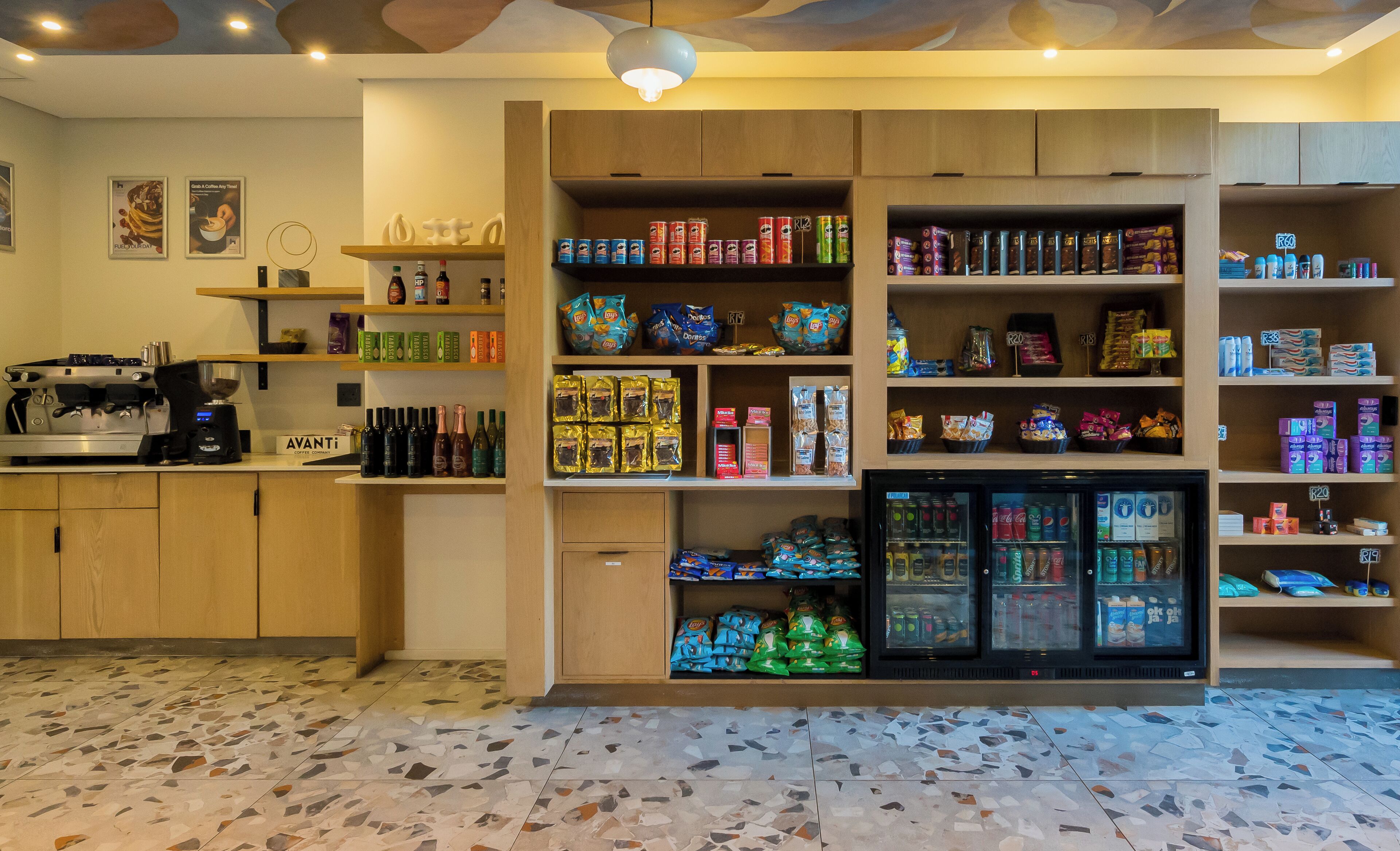 A coffee shop interior with a coffee machine, shelves stocked with snacks, and a refrigerated display.