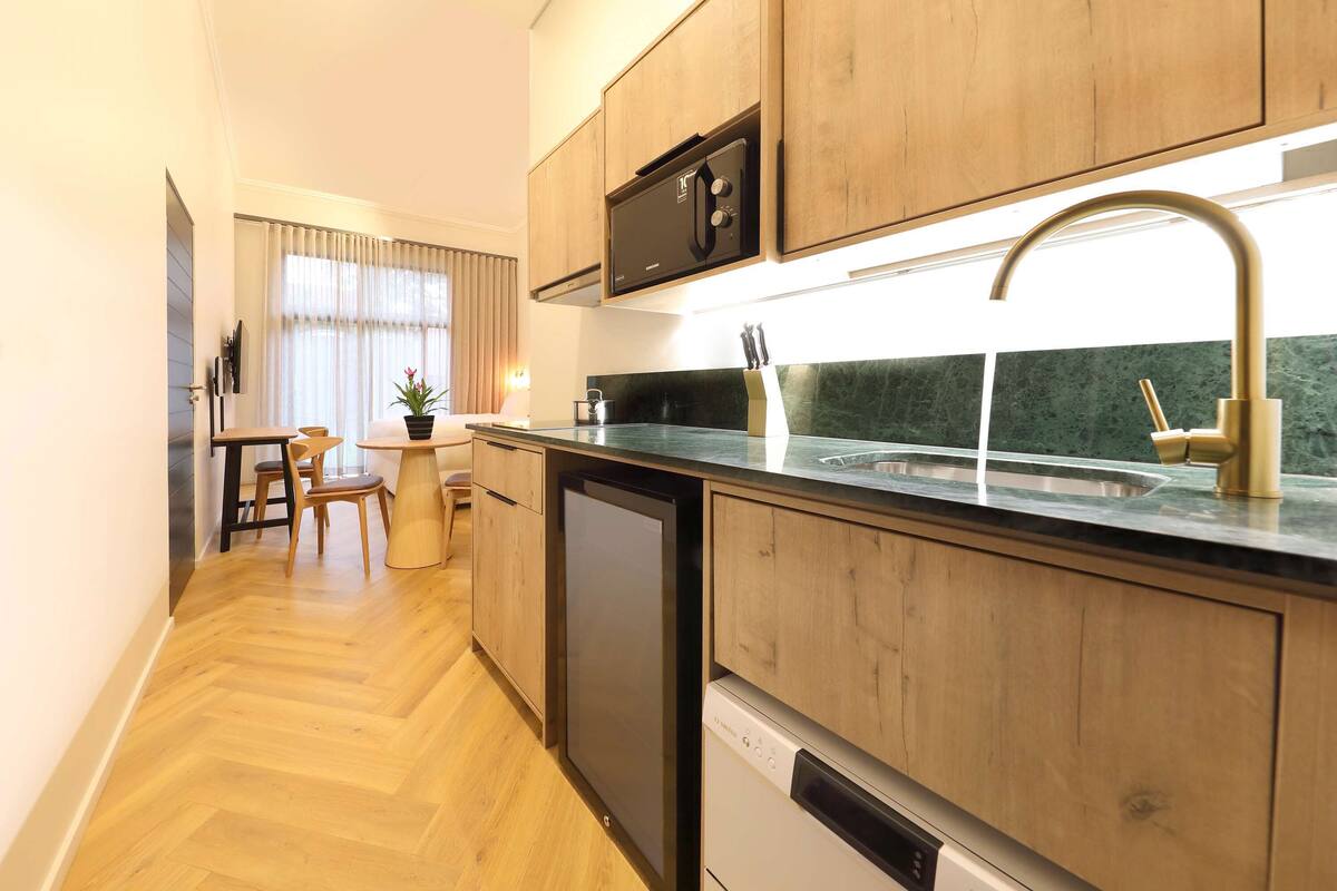 Una cocina moderna con armarios de madera, microondas integrado, lavavajillas y pileta de acero inoxidable.