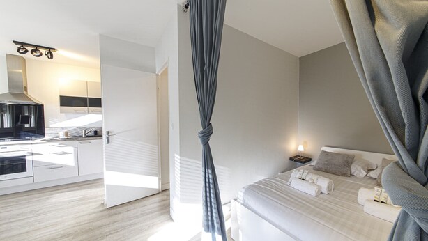 Ein modernes Hotelzimmer mit Bett, Nachttisch und Blick auf den Küchenbereich.
