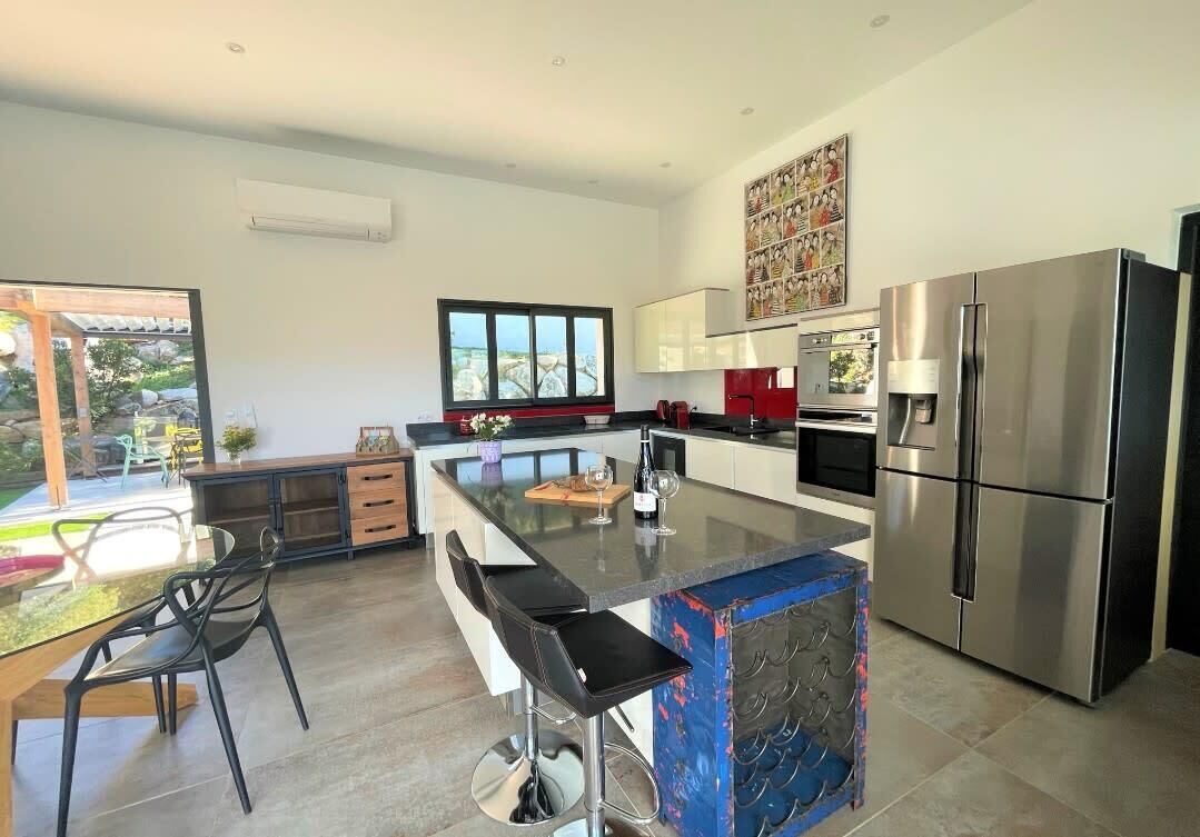 A modern kitchen with a central island, stainless steel appliances, and a large window.