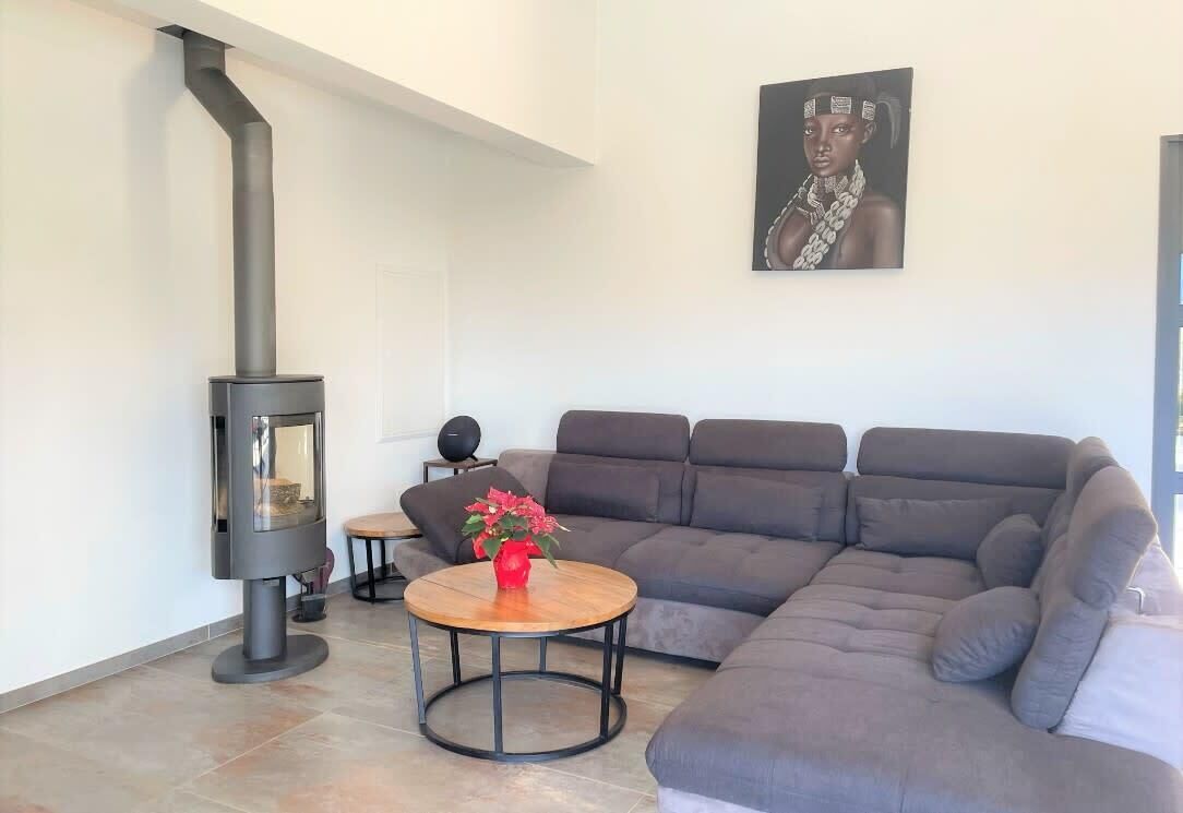 Una sala de estar moderna con un sofá modular, una mesa de centro redonda de madera, una chimenea negra y un cuadro enmarcado en la pared.