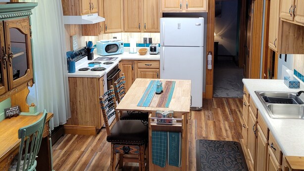 Eine rustikale Küche mit Holzschränken, einem Esstisch mit Stühlen, einem Kühlschrank und einer Uhr an der Wand.