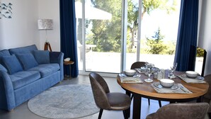 Ein modernes Wohnzimmer mit einem blauen Sofa, einem Essplatz mit Tellern und Gläsern und Blick ins Freie durch große Fenster.