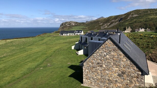 A coastal hotel with stone walls and multiple rooms, overlooking the sea.