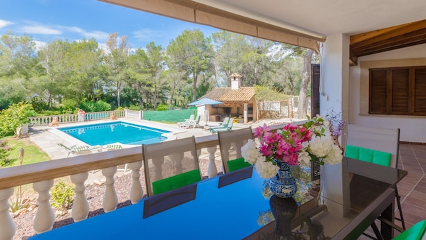 En balkon med udsigt over en swimmingpool, udendørs møbler og et bord med en blomstervase.