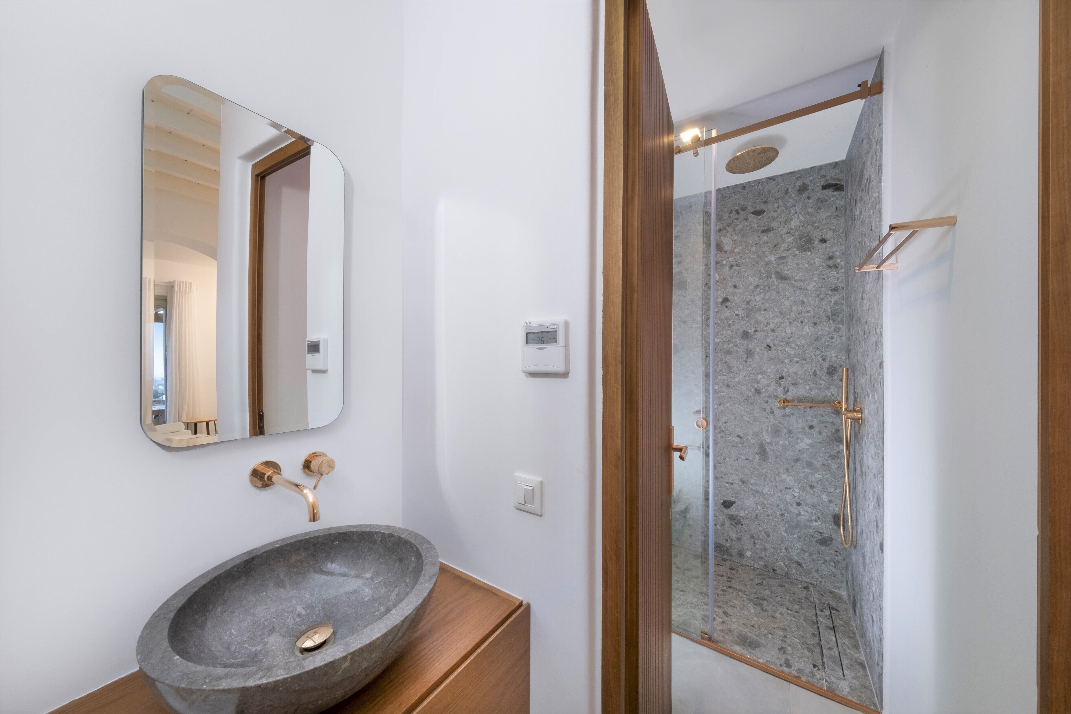 A bathroom with a stone sink, a mirror, and a shower area with a stone wall.