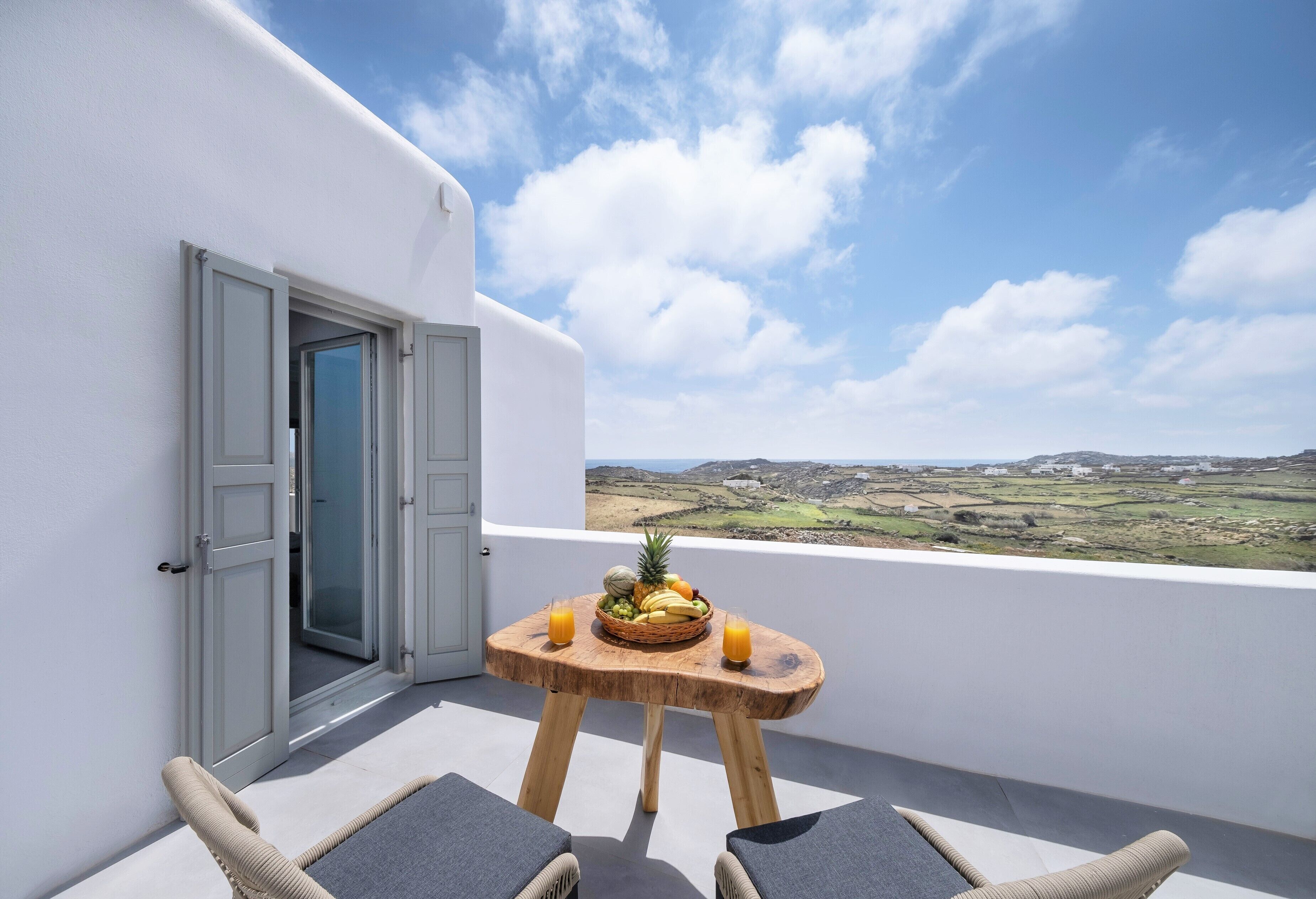 A balcony with a table set with fruit and drinks, overlooking a rural landscape.