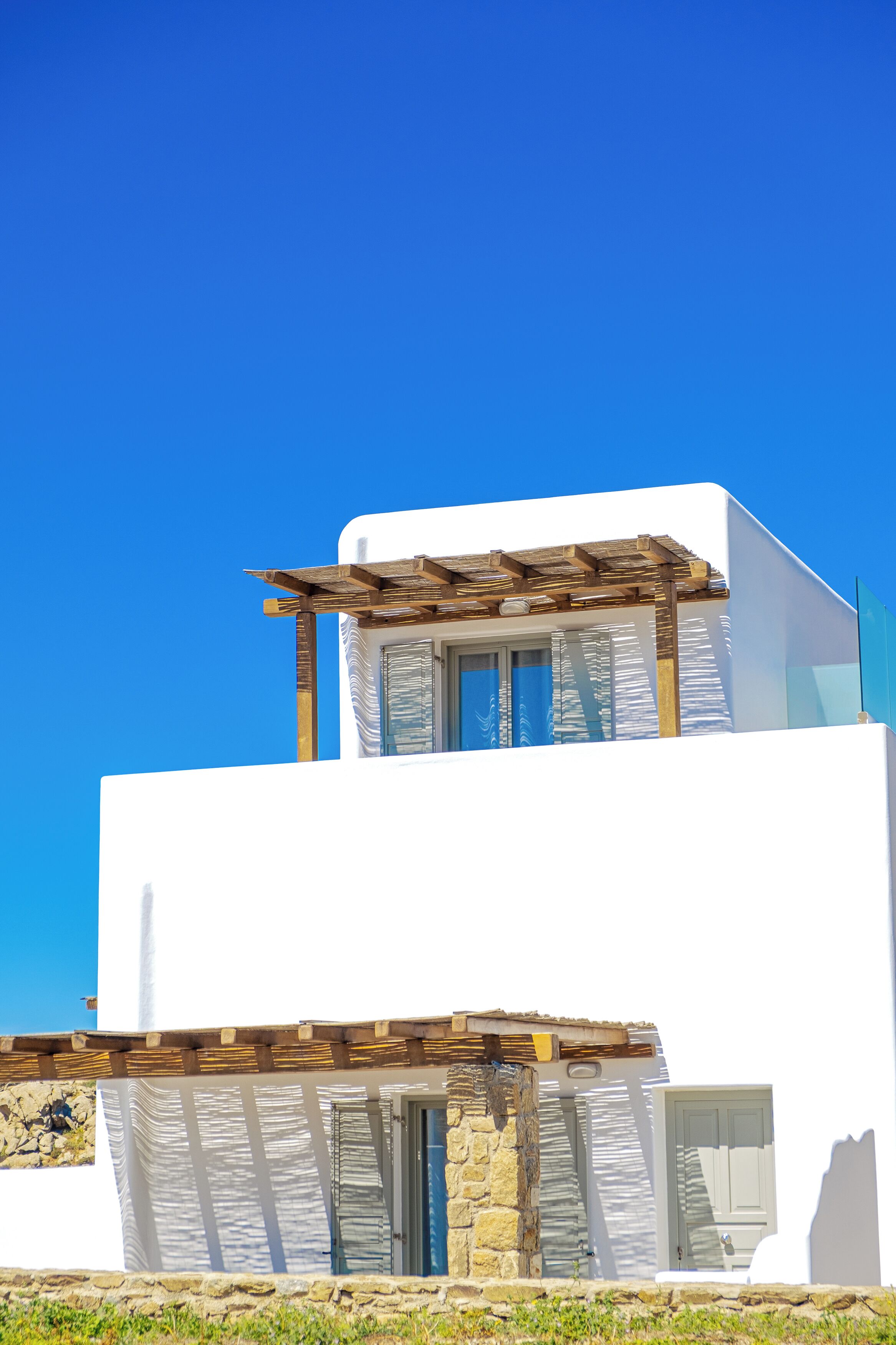 A modern white building with a wooden pergola, stone wall, and a clear blue sky.