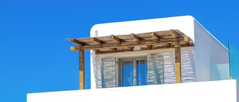 A modern white building with a wooden pergola, stone wall, and a clear blue sky.