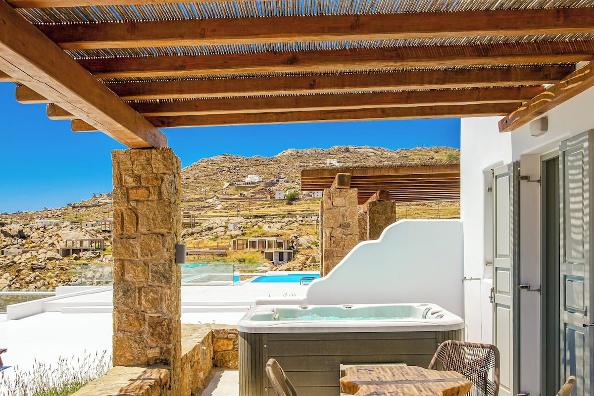 A covered outdoor area with a stone pillar, a hot tub, and wicker furniture.