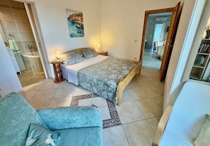 Un dormitorio con cama, mesita de noche, lámpara y un cuadro en la pared.
