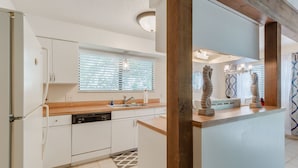 A modern kitchen with white cabinets, a wooden countertop, a built-in dishwasher, and a window with blinds.