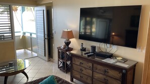 Uma sala de estar com televisão de tela plana, um armário de madeira e uma mesa de centro de vidro.