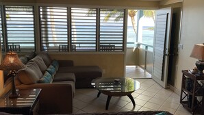 Uma sala de estar com sofá, mesa de centro de vidro e ventoinha no teto.
