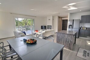 A modern kitchen with a dining area, a sofa, and a TV.