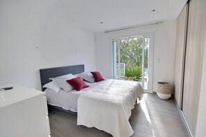 A modern bedroom with a bed, white bedding, and a view of greenery through a sliding door.