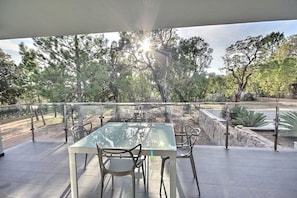 An outdoor patio with a glass table and chairs, surrounded by a stone wall and trees.