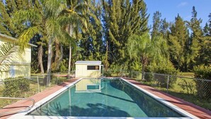 A rectangular swimming pool with a wooden deck surrounding it, a small utility shed, and a chain-link fence. - Pine Island Tropical Retreat 4 (Saint James City)