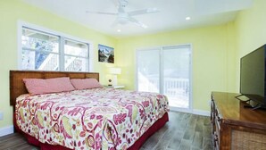 A bedroom with a bed, a nightstand, a TV, and a balcony view. - Pine Island Tropical Retreat 1 (Saint James City)