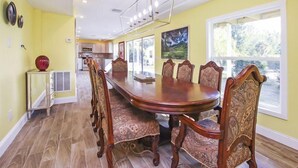 A dining area with a long wooden table and ornate chairs, a chandelier, and a view through large windows. - Pine Island Tropical Retreat 1 (Saint James City)